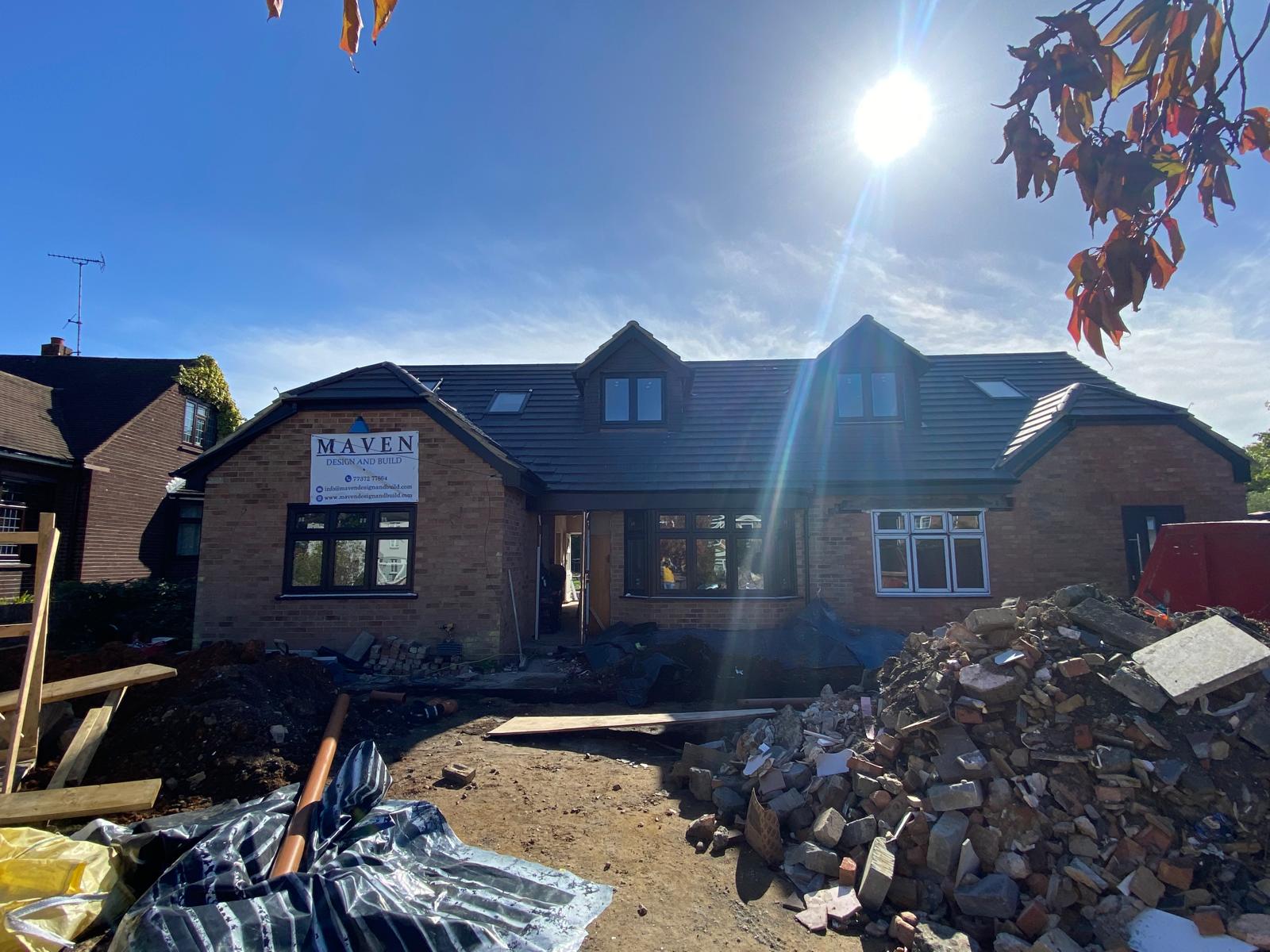 Rear extension under construction: pitched roof, structural steel above wide glazing, and roofers on site